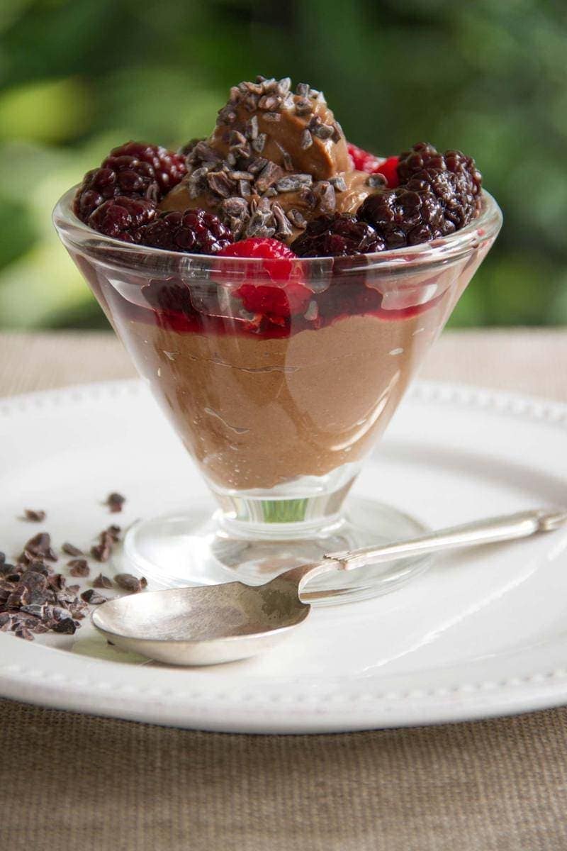 A vegan chocolate avocado mousse in a glass sundae dish, topped with fresh berries and cacao nibs