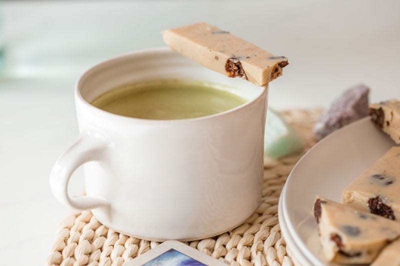 A mug of matcha tea on a coaster with a shard of homemade cookies and cream white chocolate bark resting over the top