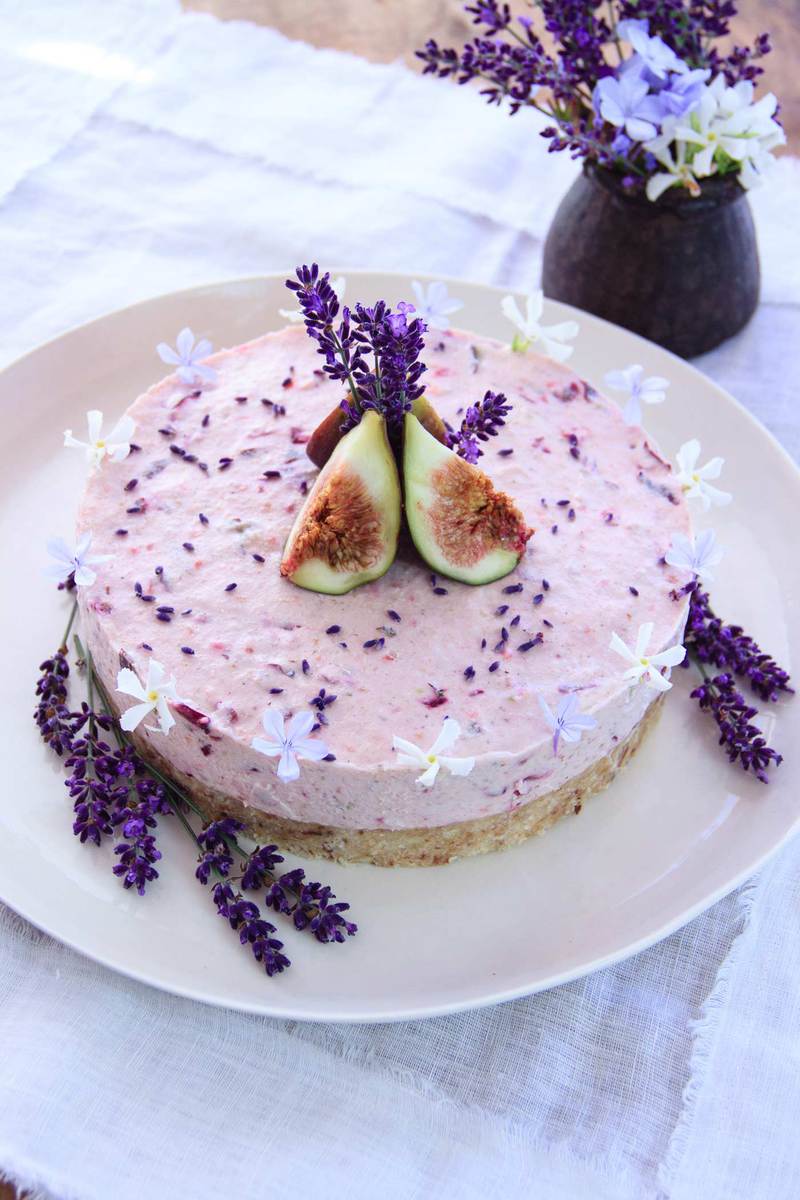 A raw Lavender Cake on a platter decorated with fresh figs and flower petals, on a rustic table