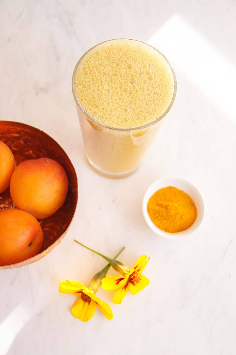 Turmeric fruit smoothie in a glass beside a bowl of apricots