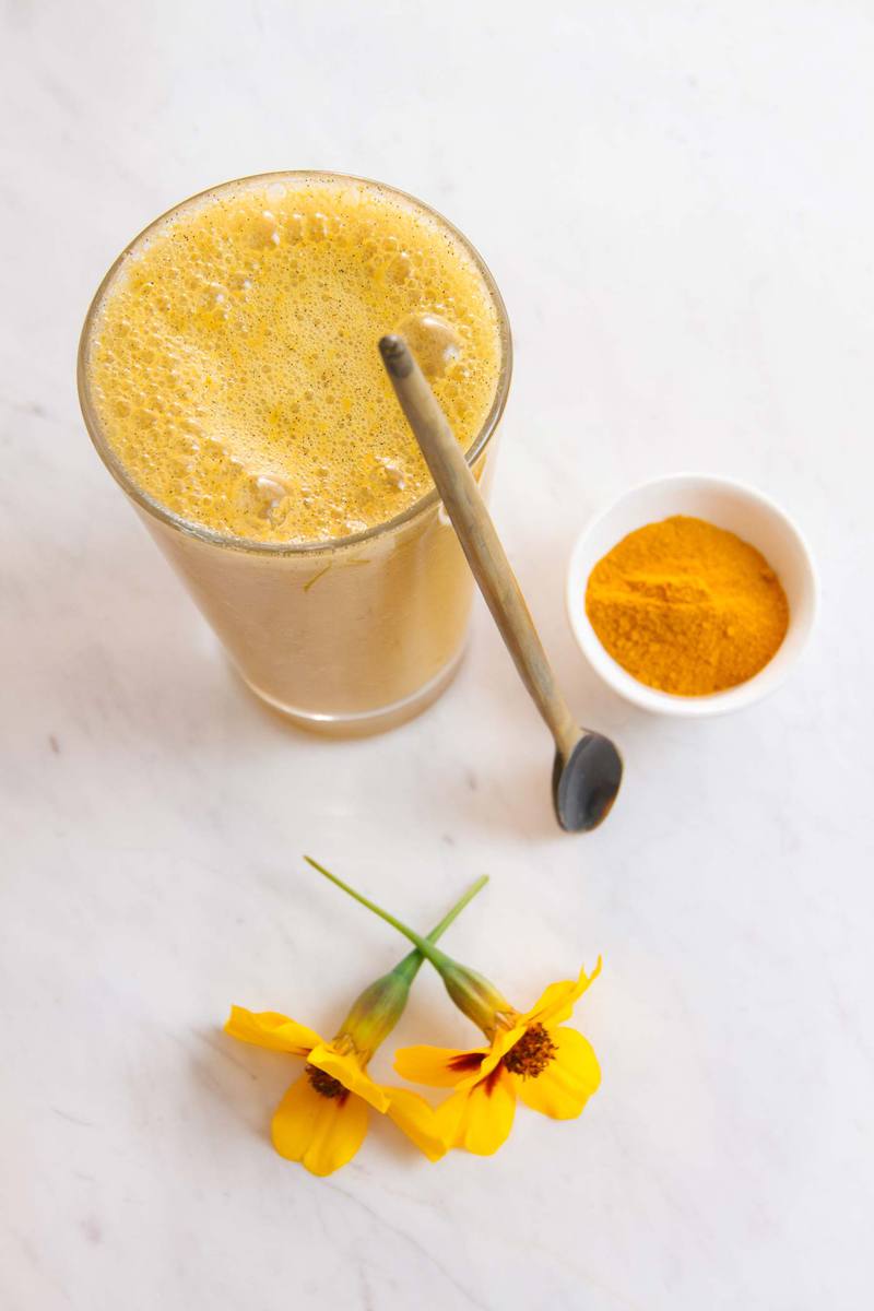 Turmeric smoothie in a glass with a spoon beside it, on the kitchen benech