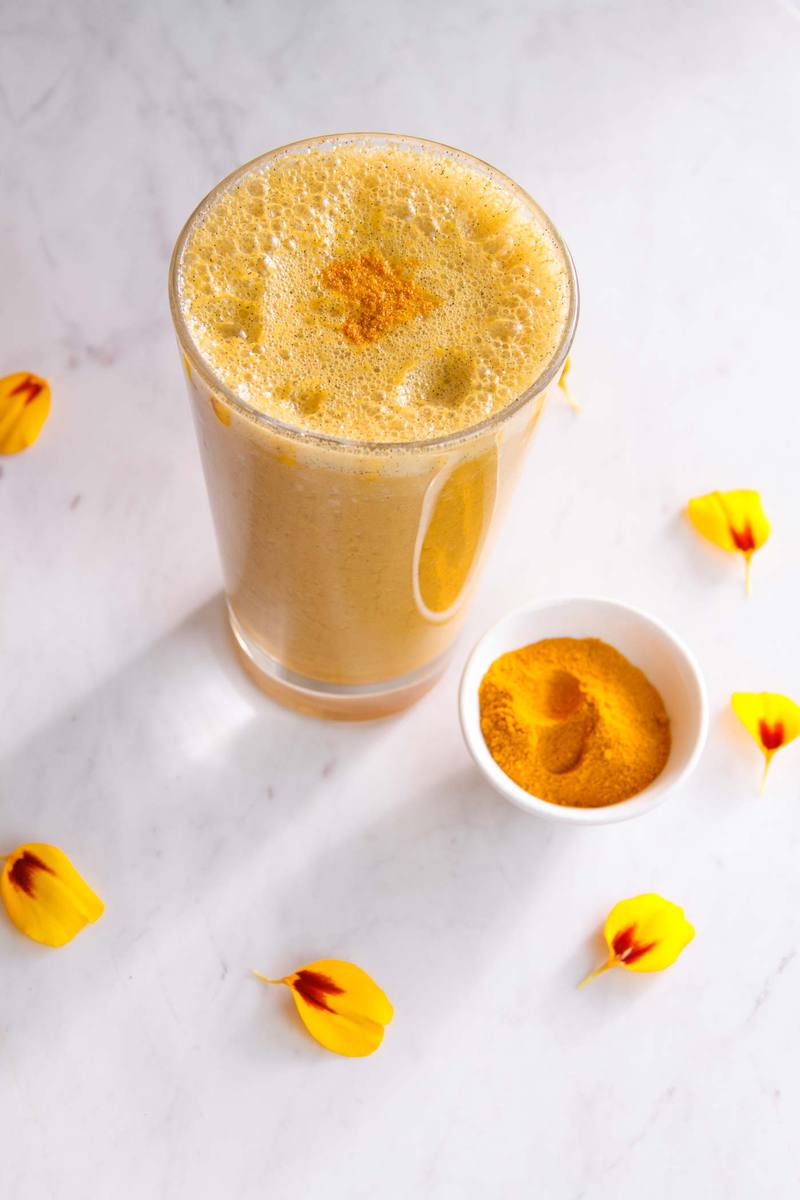 Turmeric fruit smoothie in a glass surrounded by flower petals