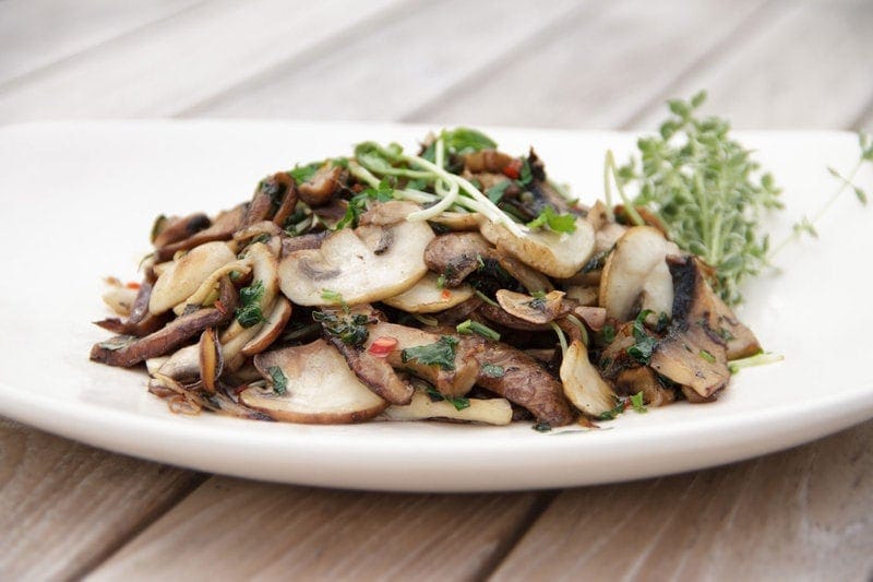 A plate of thinly sliced and cooked mixed mushrooms with ample chilli and fresh herbs on the outdoor dining table