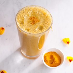 Bright yellow smoothie in a glass with a dusting of turmeric powder on top