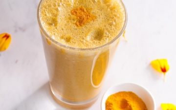 Bright yellow smoothie in a glass with a dusting of turmeric powder on top