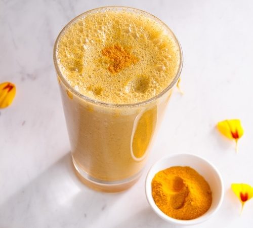 Bright yellow smoothie in a glass with a dusting of turmeric powder on top