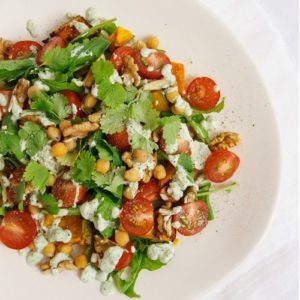 Close up of a plate of salad - pumpkin and chickpea with fresh herbs and tomatoes on top