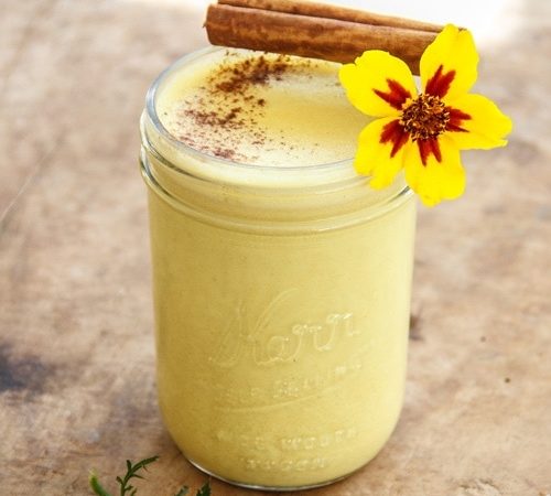 A mason jar filled with golden yellow turmeric milk and a stick of cinnamon, on a rustic wooden board