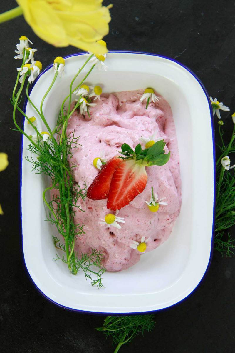 Overhead shot of an enamel dish filled with creamy pink ice cream, freshly picked chamomile on top.