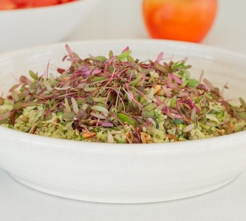 Close up of a warm quinoa salad in a white bowl, finished with a green dressing, toasted seeds and herbs