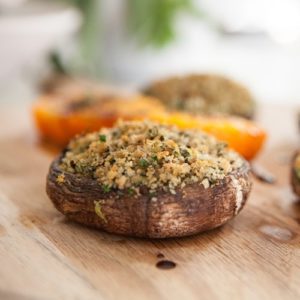 Baked mushrooms stuffed with avocado, herbs and breadcrumbs on a wooden chopping board on the kitchen bench