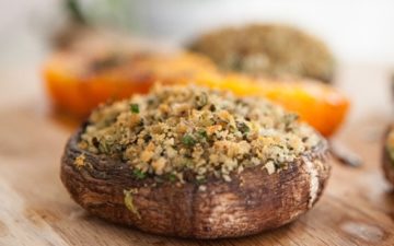 Baked mushrooms stuffed with avocado, herbs and breadcrumbs on a wooden chopping board on the kitchen bench