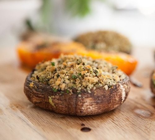 Baked mushrooms stuffed with avocado, herbs and breadcrumbs on a wooden chopping board on the kitchen bench