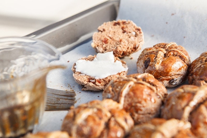 A tray of freshly baked vegan hot cross buns cut in half and slathered with coconut butter