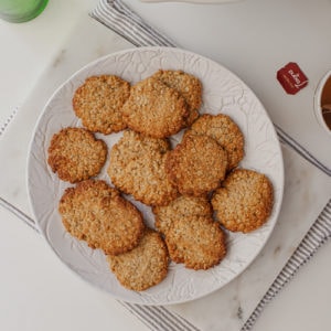 Stack of healthy ANZAC biscuits on a plate with a hot drink