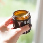 Lauren's hand holding an open jar of homemade comfrey salve