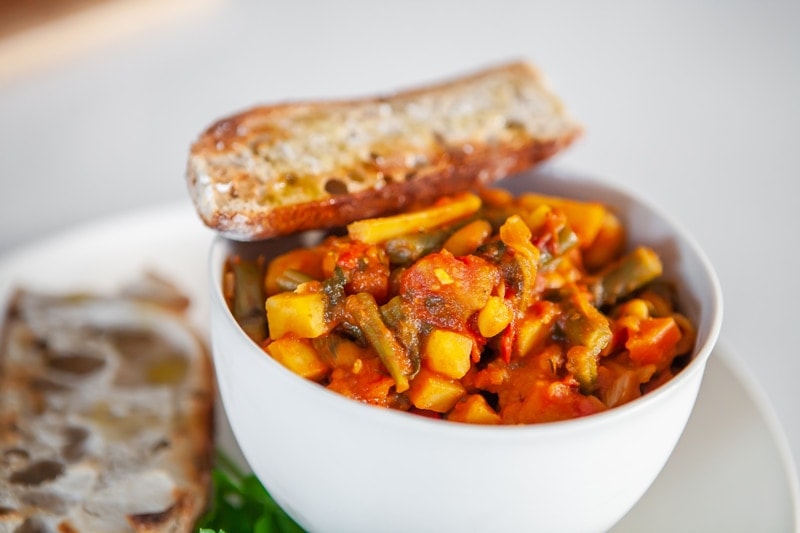 Close up of a bowl of root vegetable stew, with a piece of toasted sourdough balanced over the top