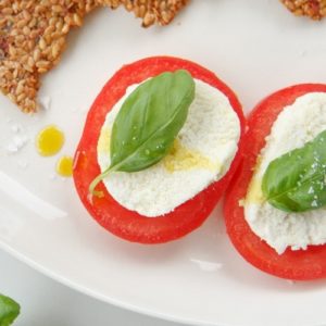 Close up of raw vegan mozzarella slices on thick sliced heirloom tomatoes topped with basil