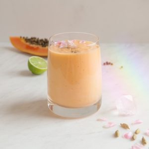Glass of orange coloured papaya smoothie on the kitchen bench