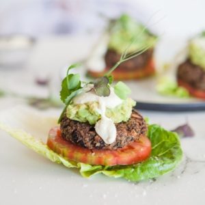 A vegan burger patty encased in a cos lettuce leaf in place of a bread bun, with tomato and dairy free aioli