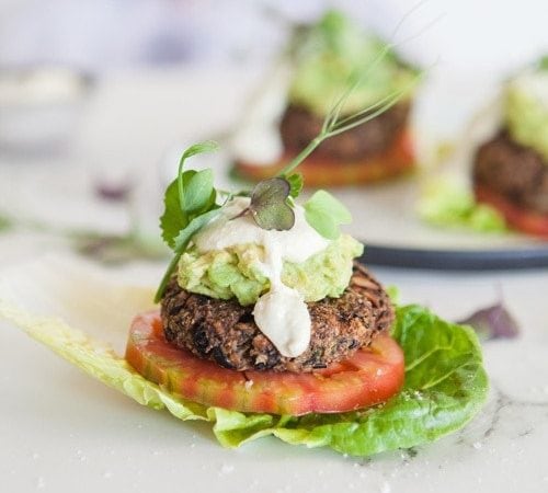 A vegan burger patty encased in a cos lettuce leaf in place of a bread bun, with tomato and dairy free aioli