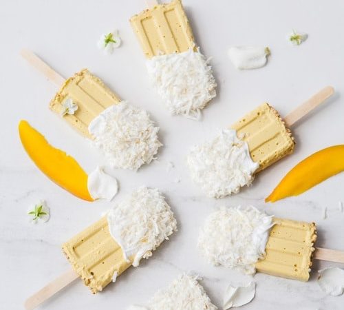 6 mango popsicles dipped in coconut yoghurt spread out over a marble counter