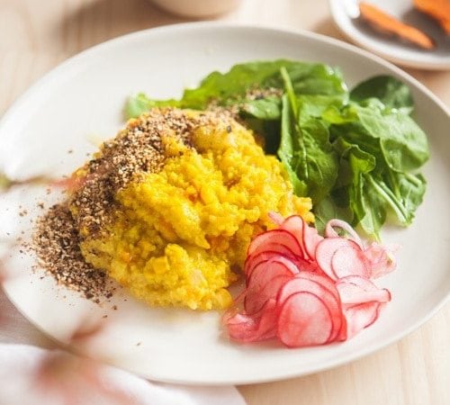 Plate filled with millet stained yellow from turmeric, with fresh greens and pickled radish