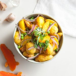 Bowl of roasted baby potatoes dyed yellow from turmeric on the kitchen bench top