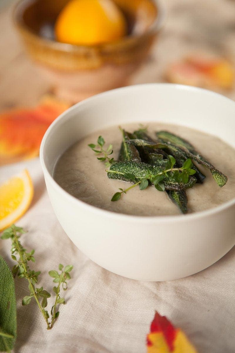Close up, vertical shot of a creamy bowl of soup in a white ceramic bowl, detailing the thick texture and herbs on top