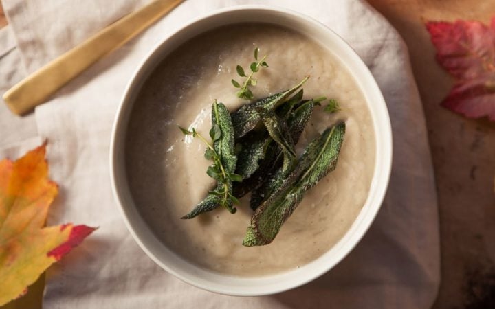 Creamy bowl of soup seasoned with fresh herbs, a golden spoon beside it
