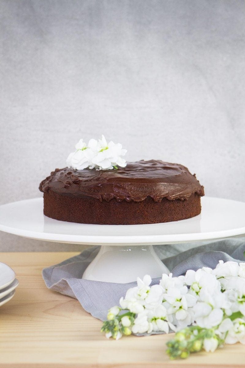 Iced Vegan Chocolate Cake on a white cake stand with white flowers