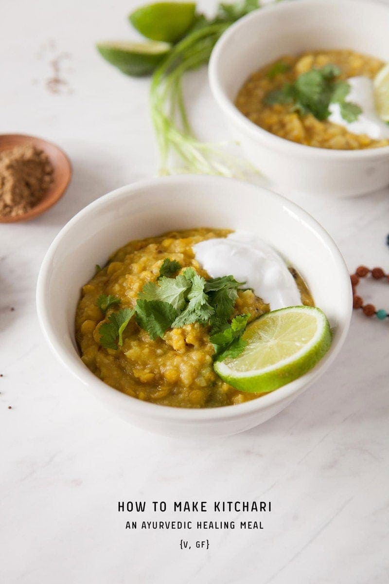 Beautifully styled bowl of kitchari on a kitchen bench, surrounded by fresh herbs, cut lime, spices in pinch bowls. The recipe title is printed over the top, for pinterest pinners.