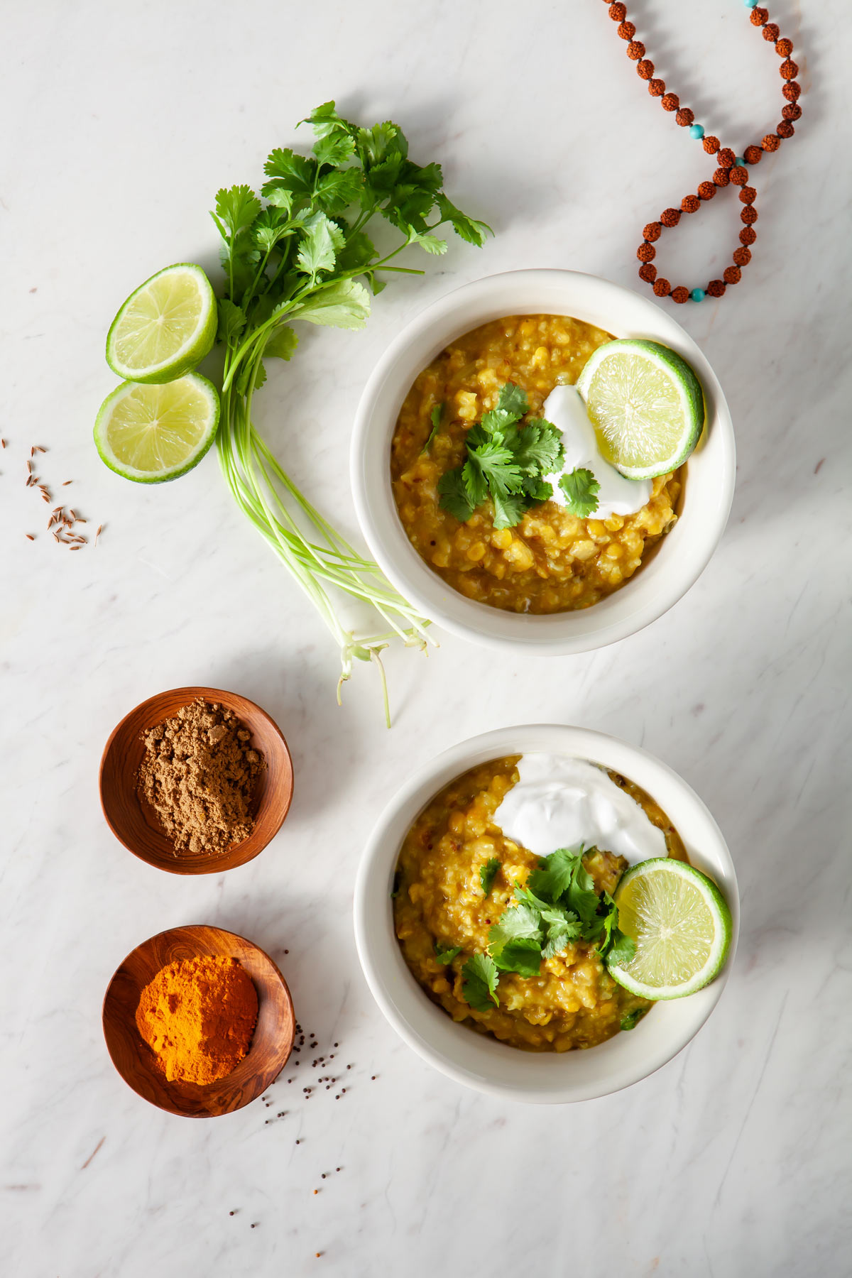 Two beautiful bowls of healing Kitchari - also known as Khichdi - with spices and fresh coriander root beside them