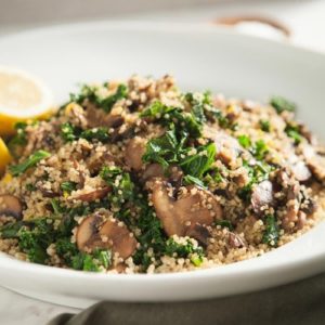 Close up of warm quinoa salad in a white bowl with fresh herbs