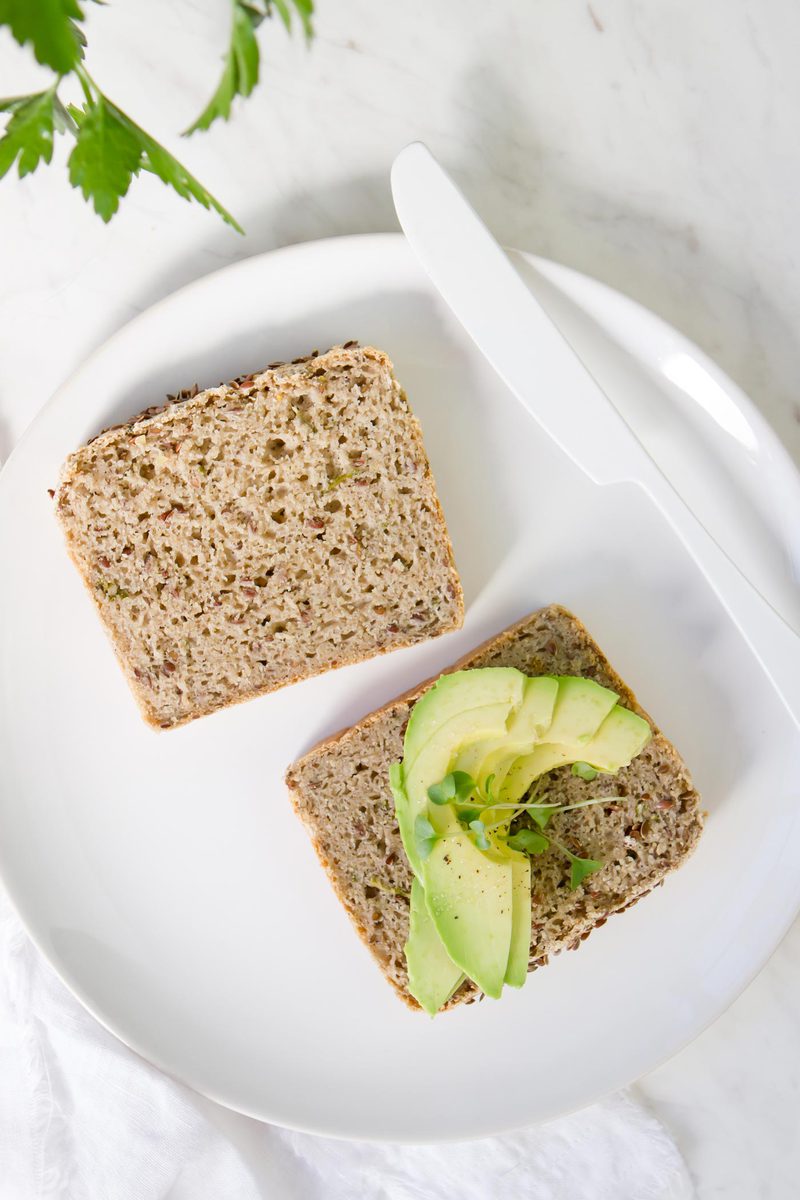 Two slices of spongy homemade bread on a white plate, with a few slices of avocado on one piece