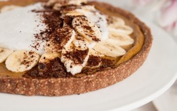 Close up of a vegan banoffee pie on a white cake stand with whipped coconut and chocolate shavings on top