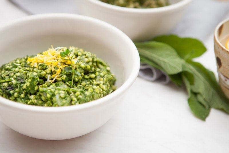 Creamy Spinach and Buckwheat Risotto topped with fresh lemon zest in a white bowl