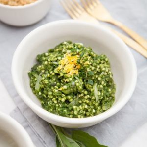 White bowl of buckwheat risotto that is bright green from the spinach, on a blue napkin