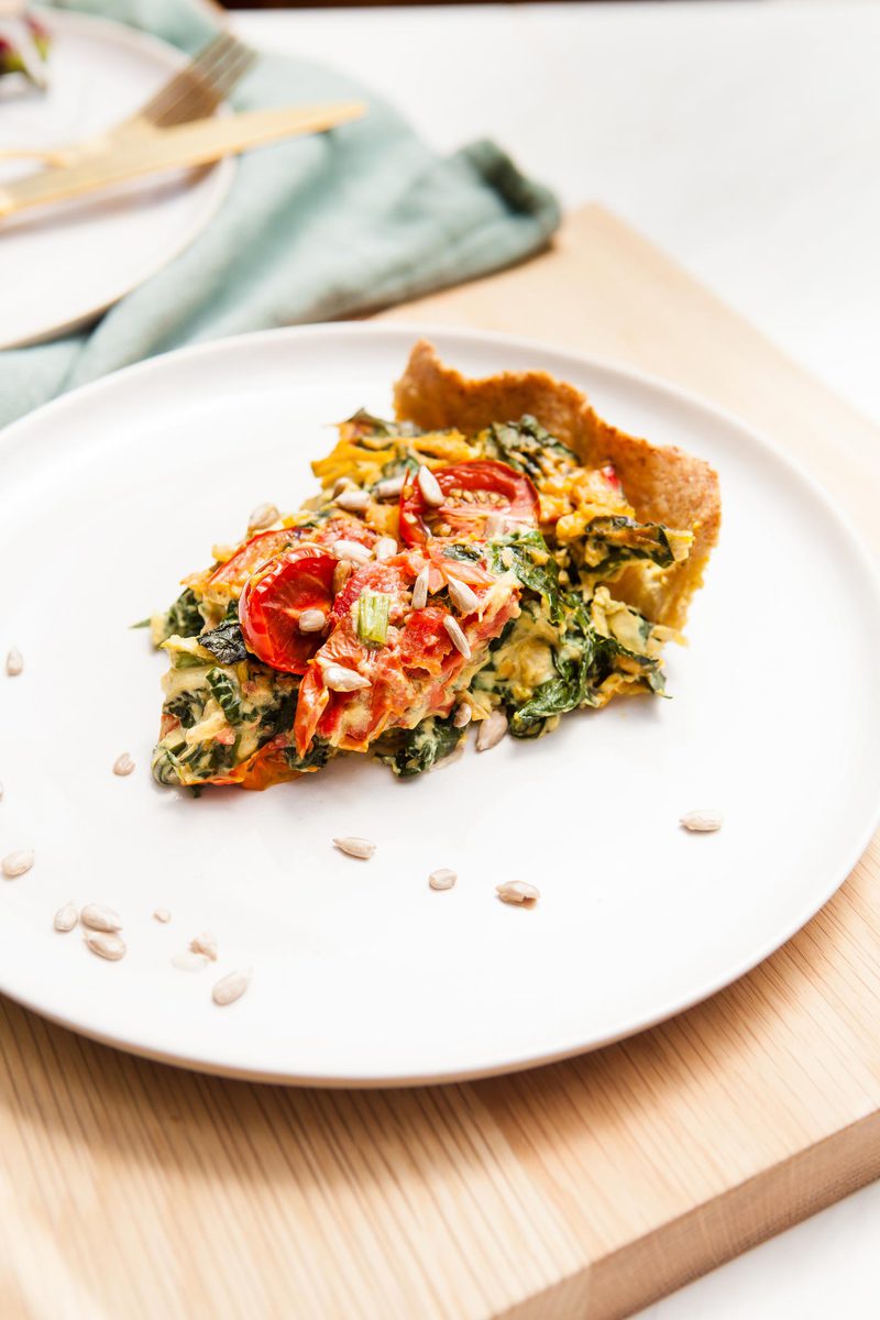 Close up of a slice of vegan gluten free quiche on a plate, with sunflower seeds sprinkled on top