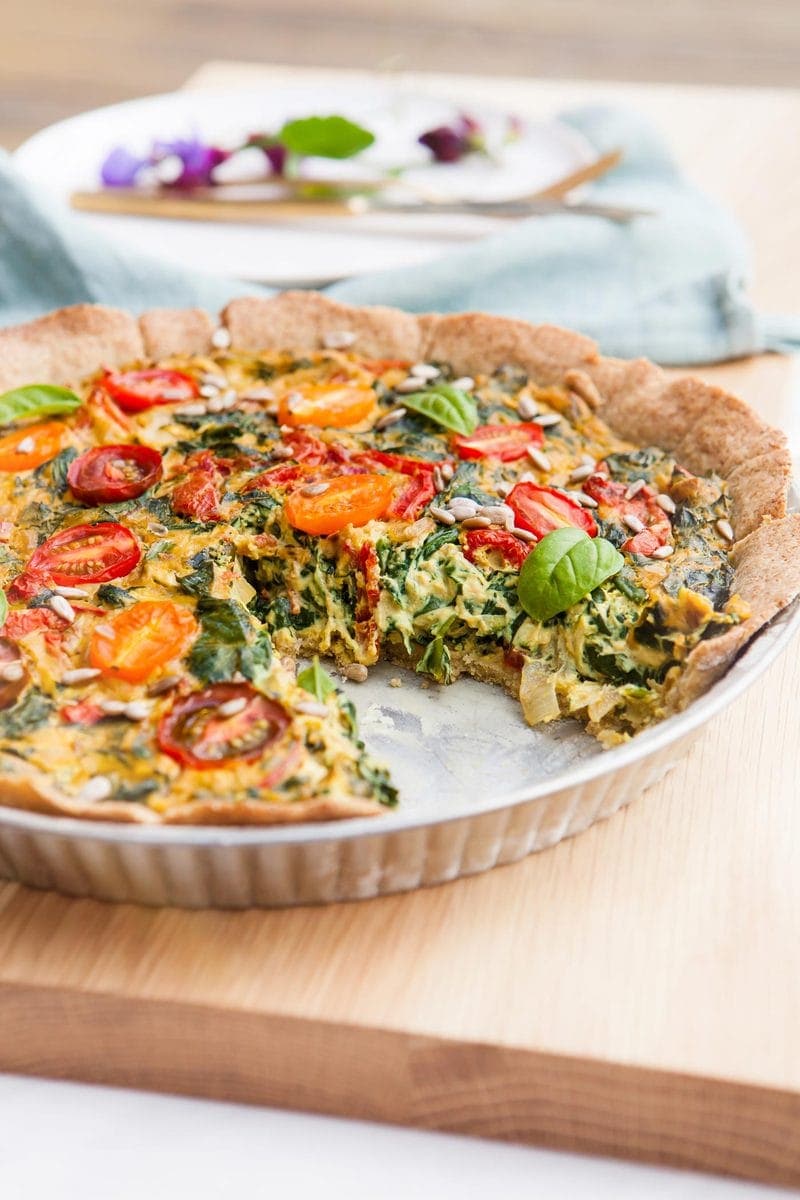 A gluten free quiche in a pie dish with a slice missing, revealing a filling packed with vegetables