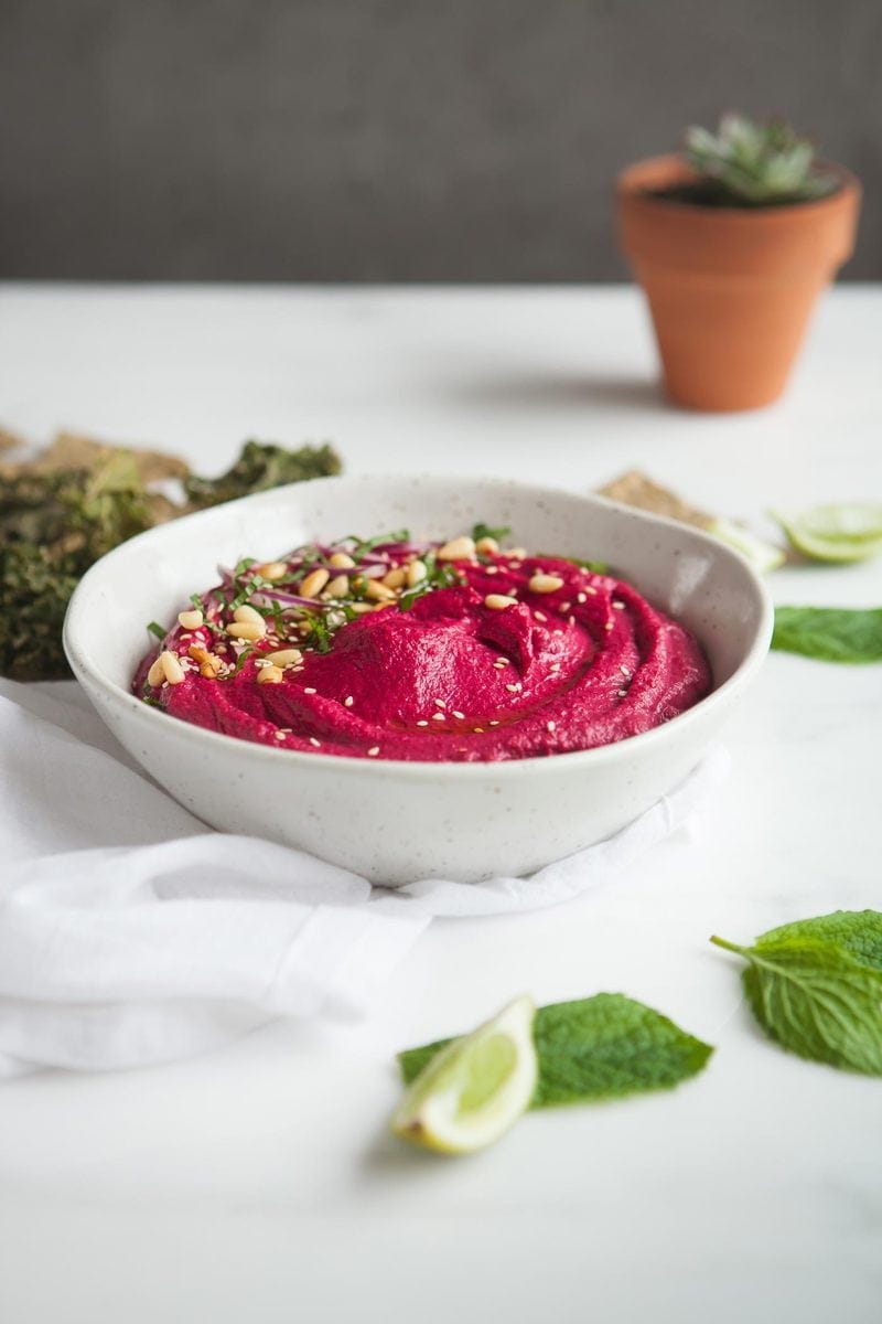 Hot pink roasted beet hummus on kitchen bench with corn chips and lime wedges