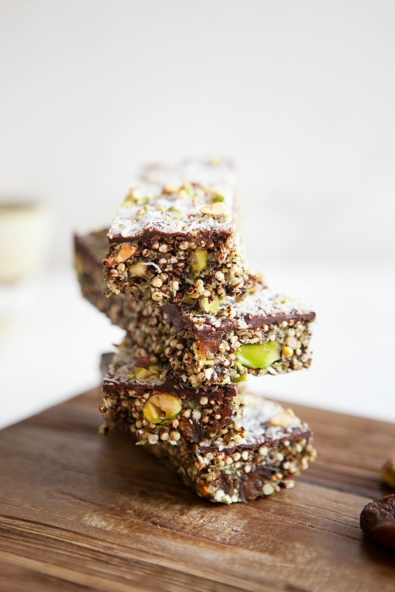 Close up of a stack of quinoa bars with chocolate topping revealing bright coloured apricots and pistachios inside