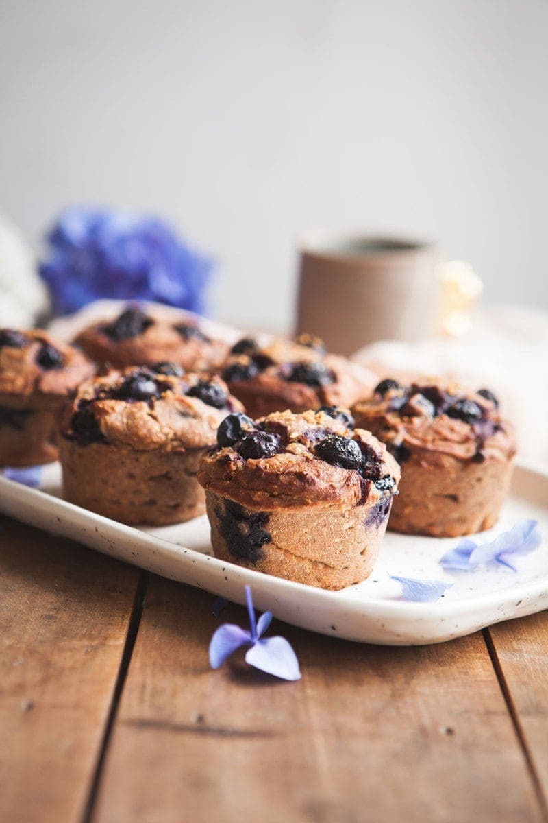 Gluten Free Blueberry Muffins made with teff on a ceramic plate with mugs of tea