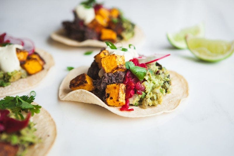 Side profile of a butternut squash taco with black beans, kraut, guacamole and scallions