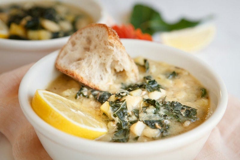 Close up of a bowl of soup with a lemon wedge and slice of rustic sourdough.