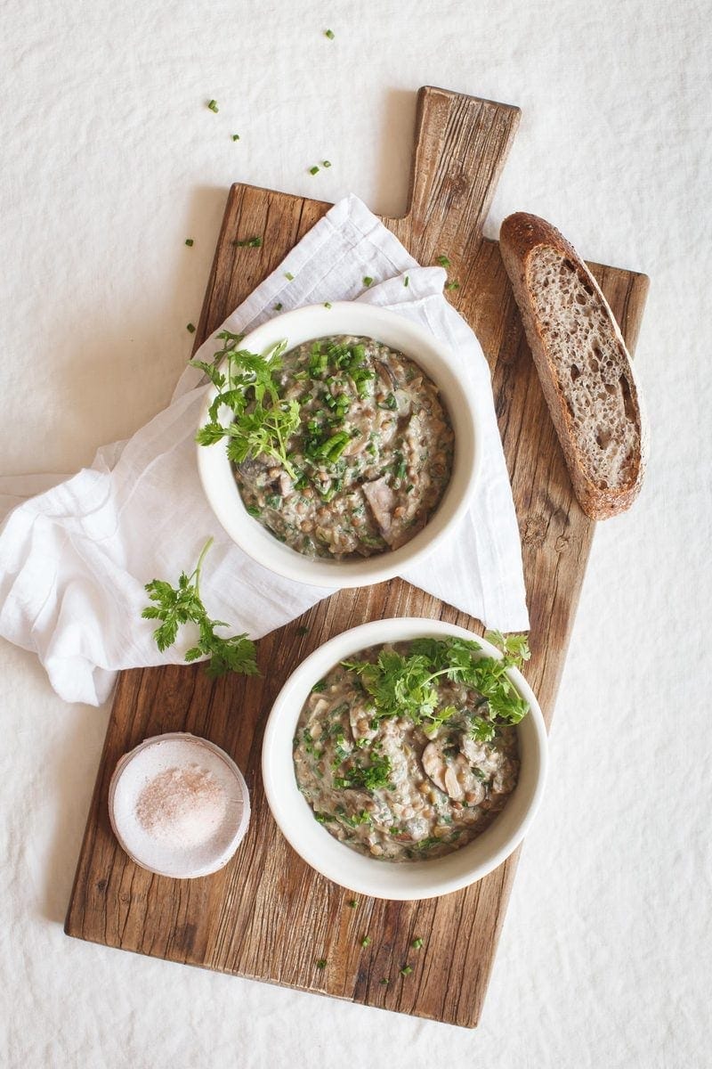 Two bowls of hot mushroom lentil stew with chunky bread next to them