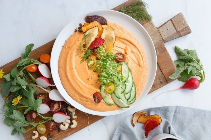 A plate filled with Chargrilled Capsicum Hummus and colourful garnishes on top