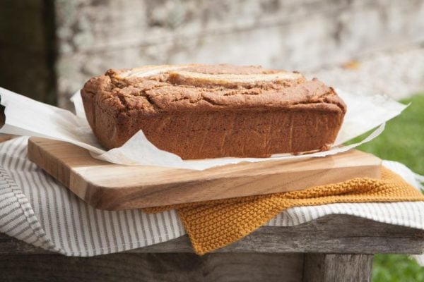 Side profile of a freshly baked loaf of gluten free vegan banana bread on a wooden board in a courtyard setting