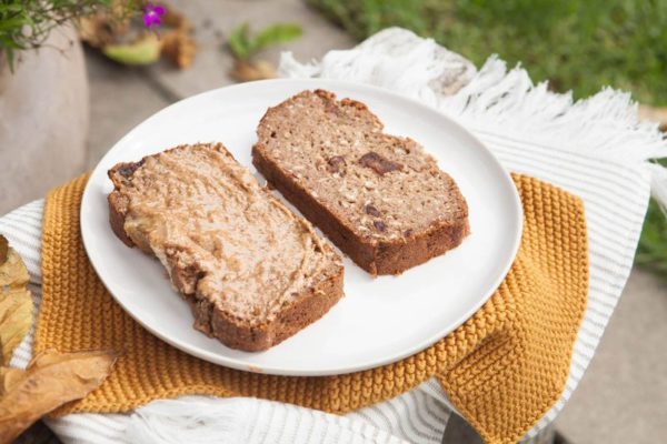 Two slices of gluten free vegan banana bread with almond butter on top, in a garden setting