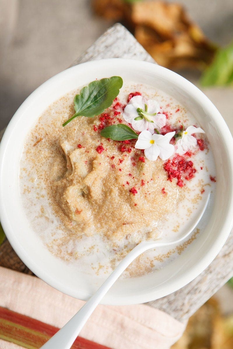 Close up of a bowl of Amaranth Porridge topped with coconut milk, freeze dried raspberries and violet flowers